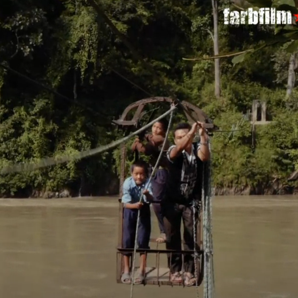 Zwei Jungs und eine Mann stehen in einer Seilbahn und fahren uüber einen Fluss. Sie ziehen sich an einem Seil an Land.