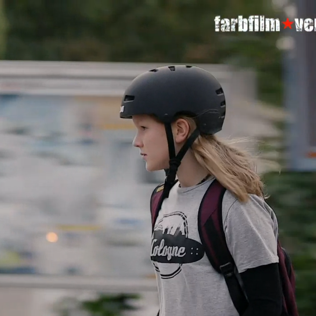 Ein Mädchen mit einem Helm fährt Skateboard.