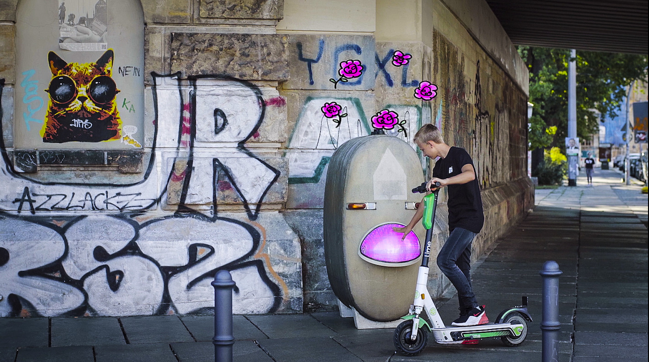 Elias steht auf einem Roller und spricht mit seiner Sprachbox Rose.
